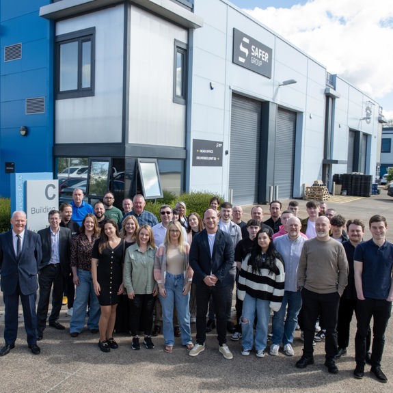 A group photo of employees and council representatives in front of the Safer Group building, showcasing diverse outfits and professional attire.