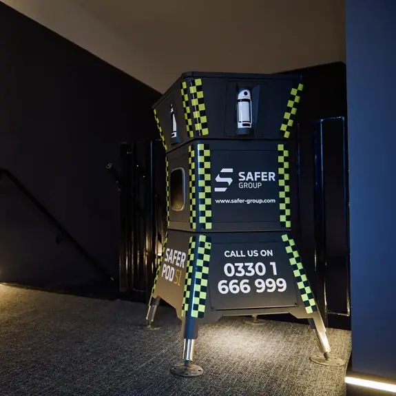 A black and yellow Safer Group Safer POD S1 stands at the top of a staircase, illuminated by soft lighting in a modern space.