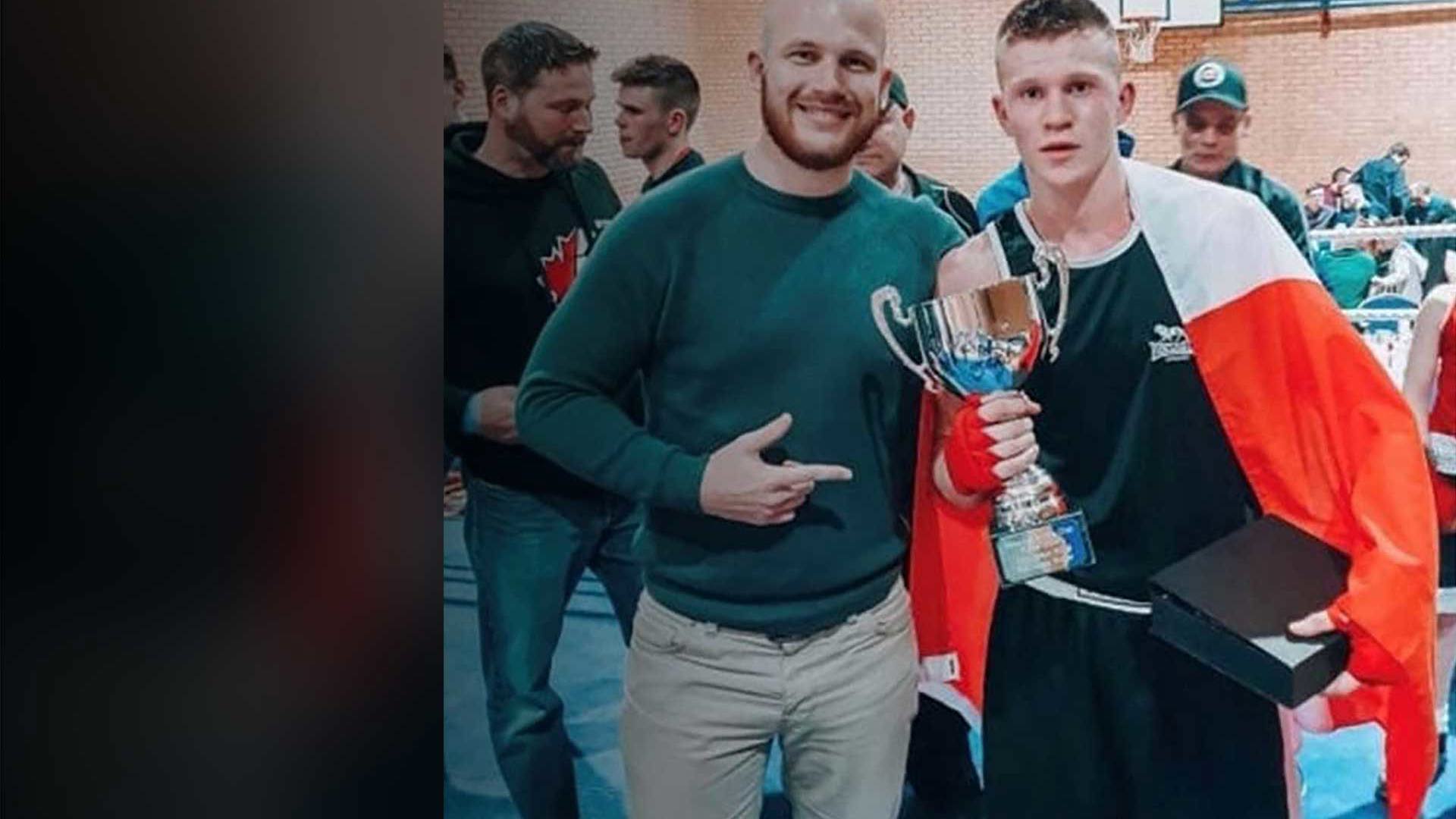 Ryan Clark joins a sponsored athlete celebrating a sports victory, with the athlete holding a trophy while draped in a flag and surrounded by others in a gym hall.