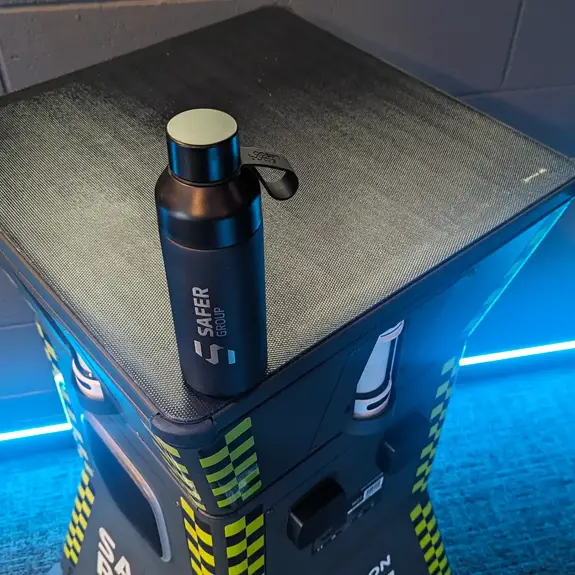 A sleek black water bottle with the "Safer Group" logo rests on a textured solar panel surface with blue LED lighting in the background.