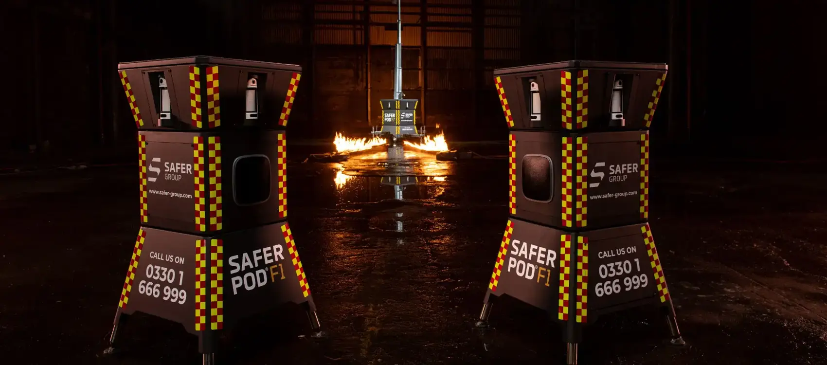 Two black safer pod F1s with yellow and red reflective patterns stand in a dimly lit space, flames flicker in the background alongside a Safer POD F7.