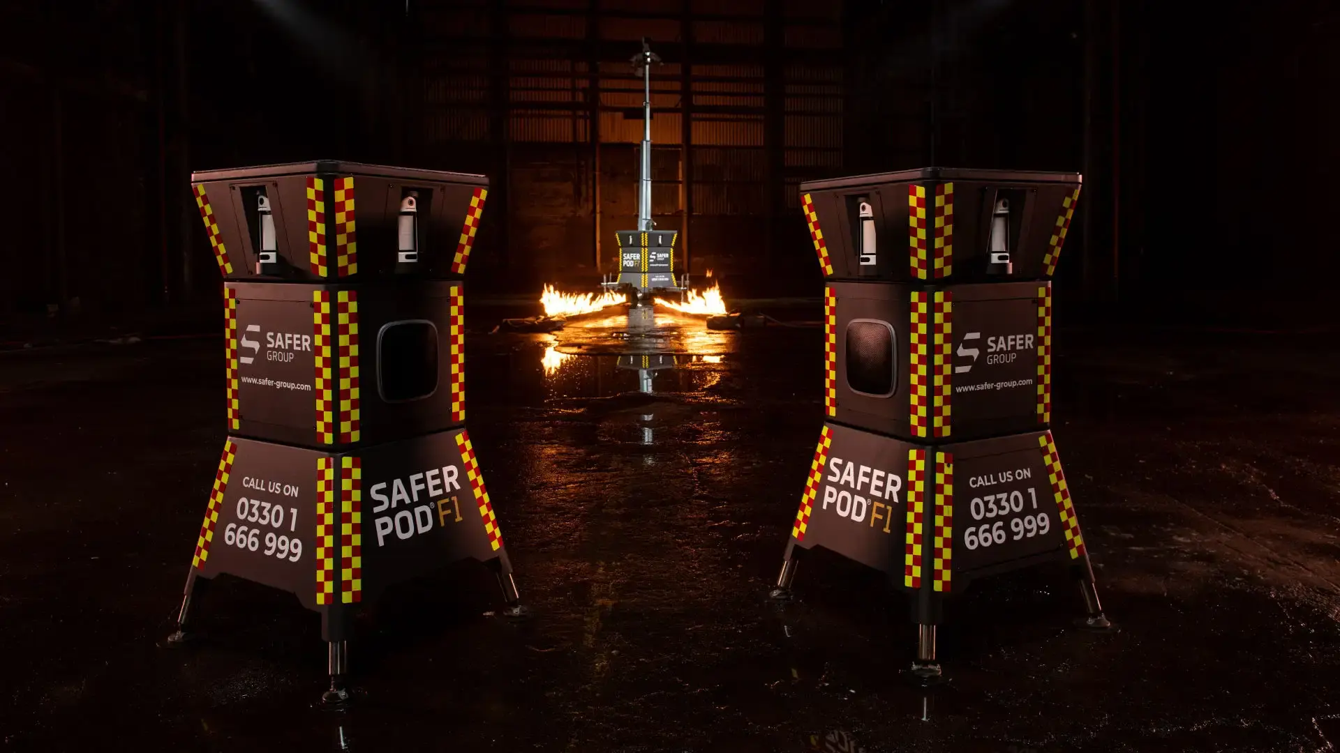 Two black safer pod F1s with yellow and red reflective patterns stand in a dimly lit space, flames flicker in the background alongside a Safer POD F7.
