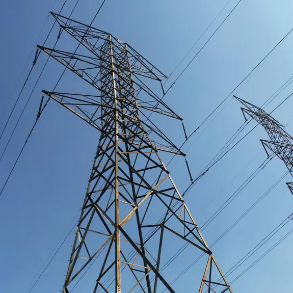 Two towering power transmission lines stretch against a bright blue sky, showcasing their metal structures and connecting wires.