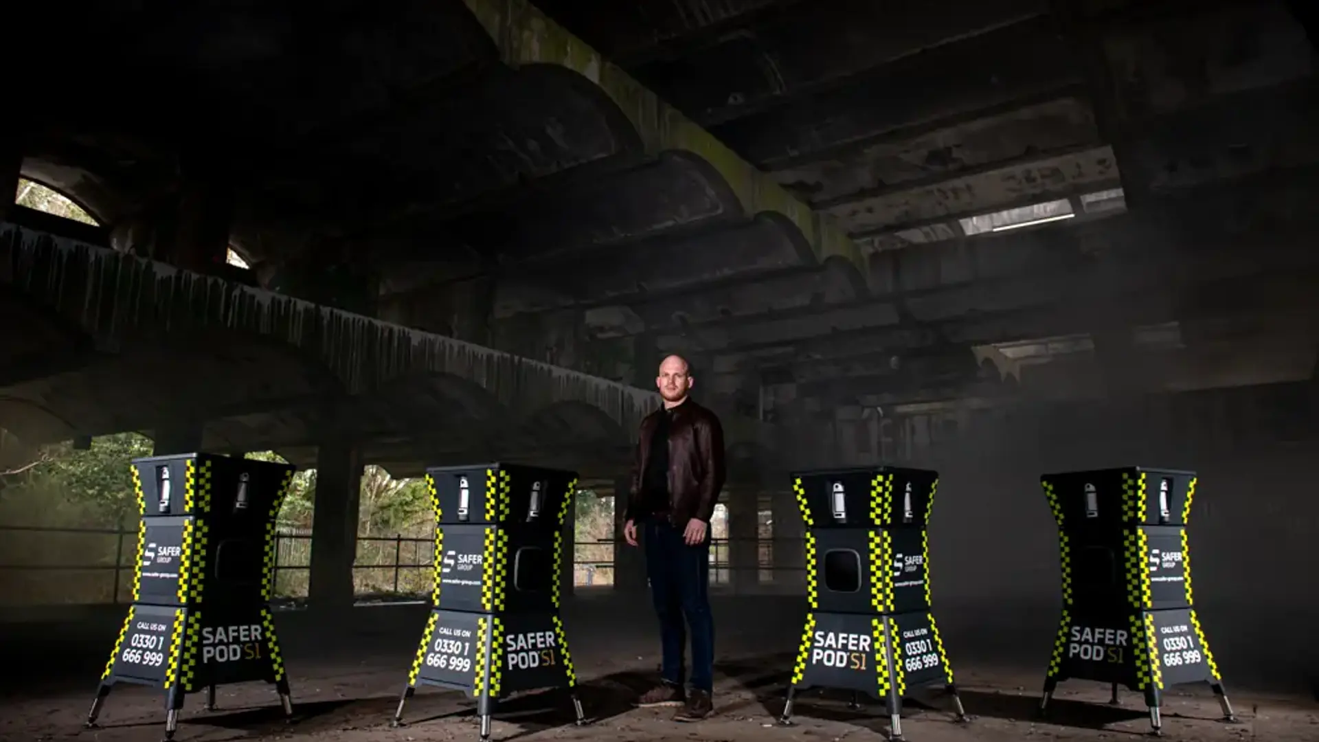 A dimly lit, abandoned building features four Safer Pod S1 devices, with Group chief executive Ryan Clark standing in the middle of them.