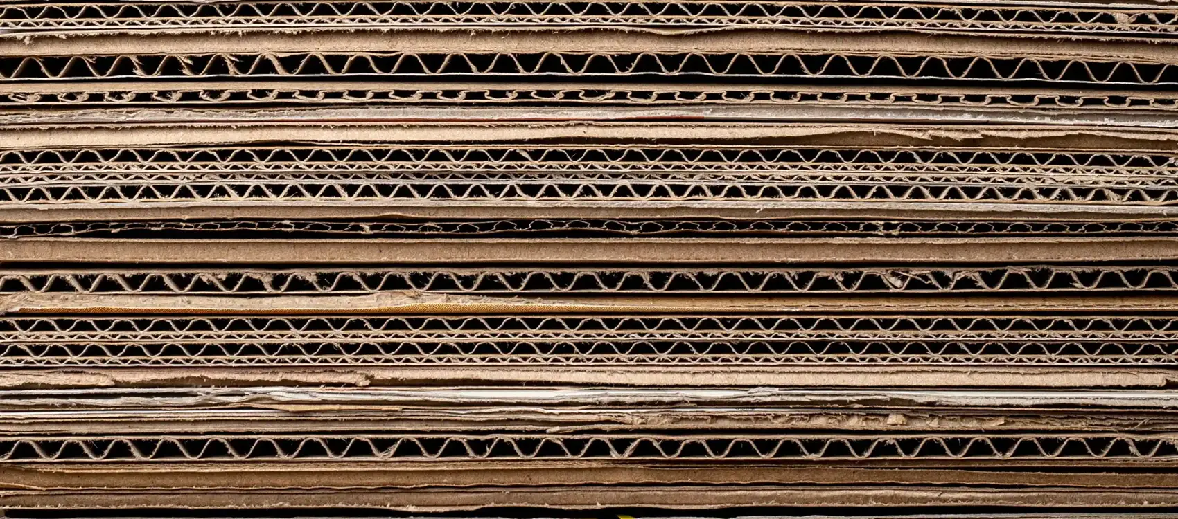 Stacked layers of cardboard with visible corrugated patterns and varying textures, creating a neutral, earthy background.