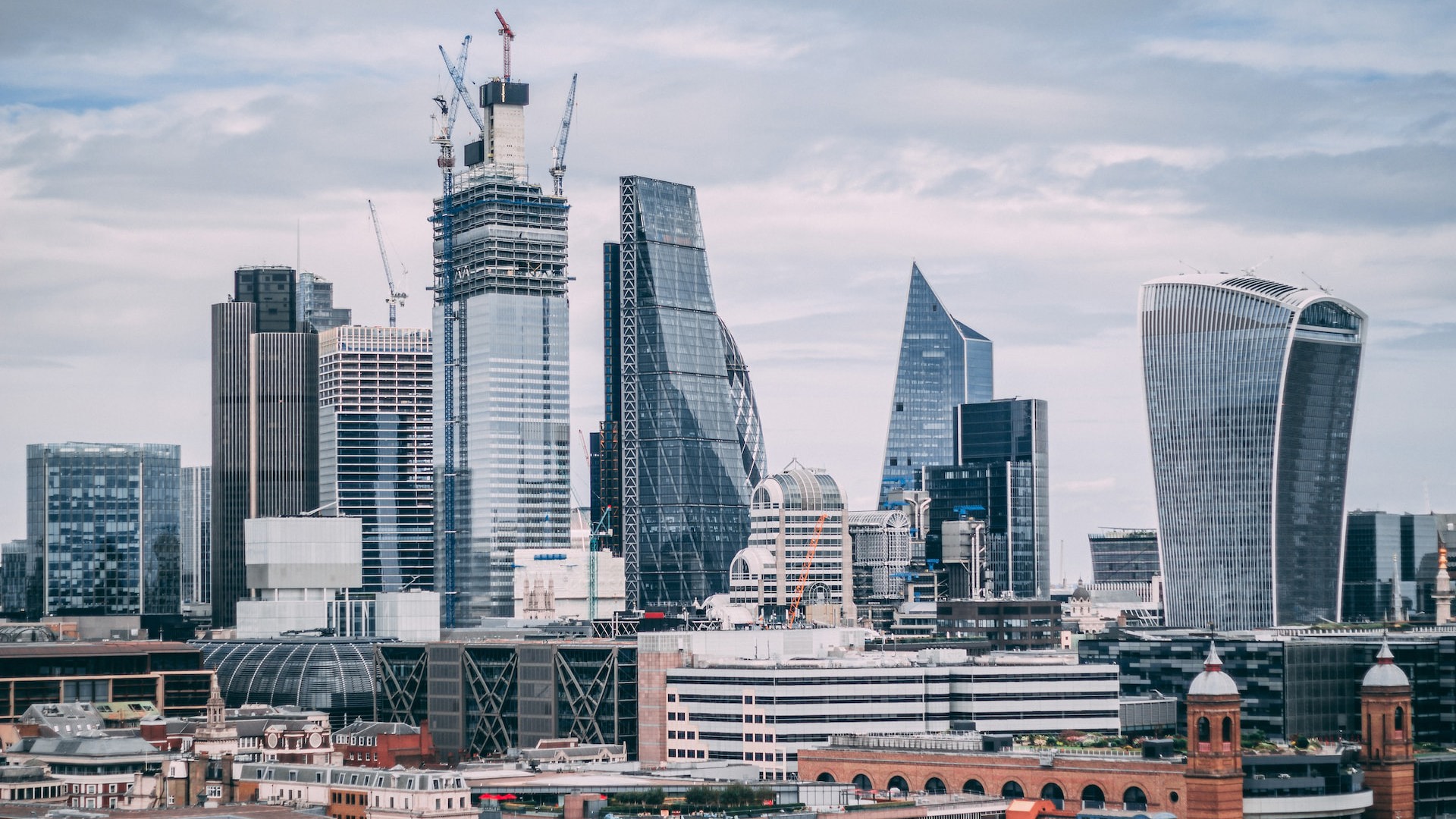 landscape of a modern busy city on a cloudy day, with old and modern architecture combined between large glass structures and older brick buildings