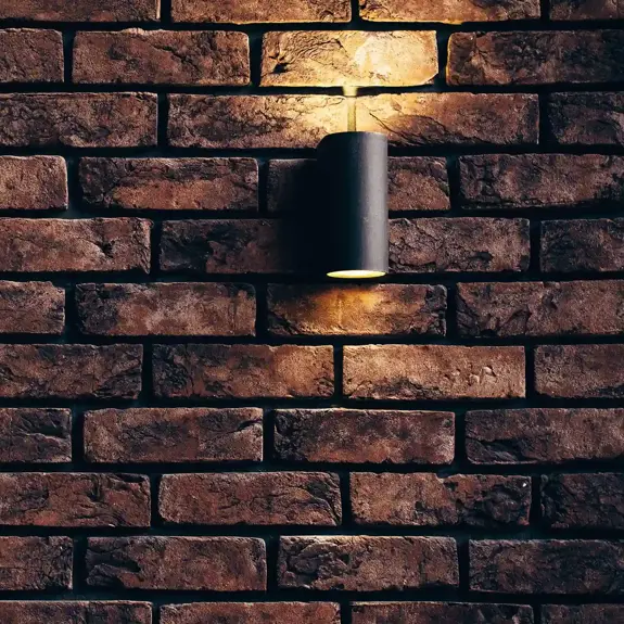 A textured, warm-toned brick wall illuminated by a minimalist black wall lamp, creating a cozy atmosphere.